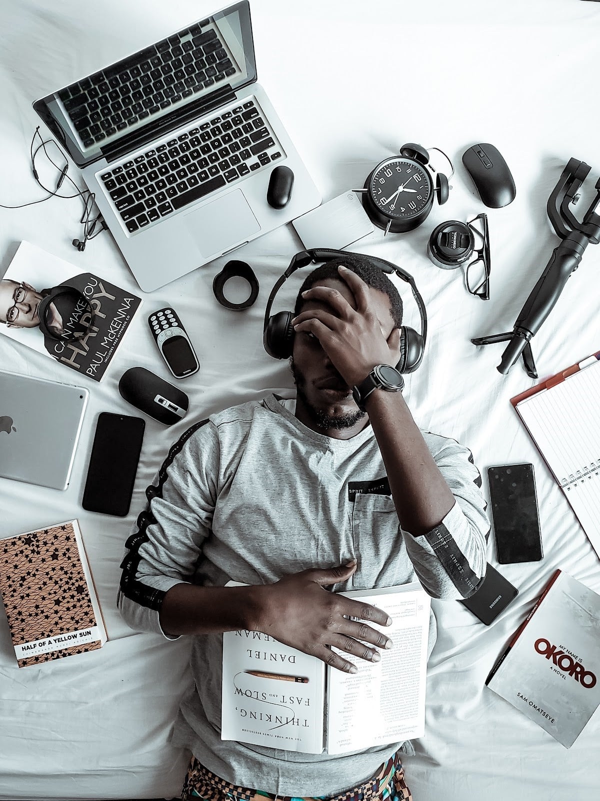 a man lying down with headphones on, surrounded by gadgets