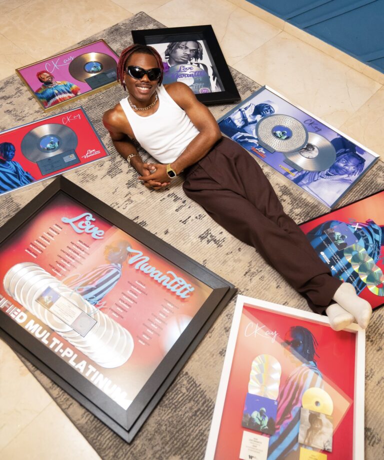 Ckay sitting surrounded by his record plaques